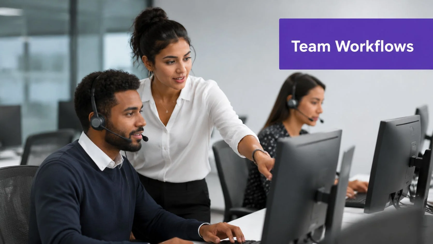 A female team lead points to a computer screen while assisting a male employee at the office.